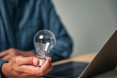 A man makes a creative hand gesture to pose with a lightbulb, a sign of a n.. Stock Photos