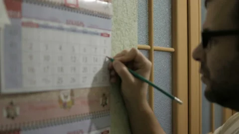 A man makes a date stamp in wall calendar. Planning a vacation. Birthday. Wor 스톡 동영상 99040141