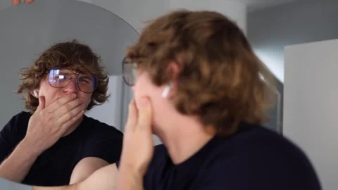 Man makes a disgusted grimace while looking at his reflection in the mirror reac Stock Footage 312981829