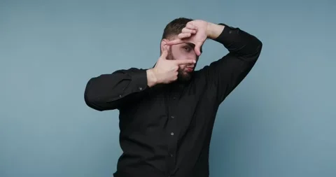 Man makes a frame gesture with hands in front of a blue background while we.. Vídeo Stock 326798584