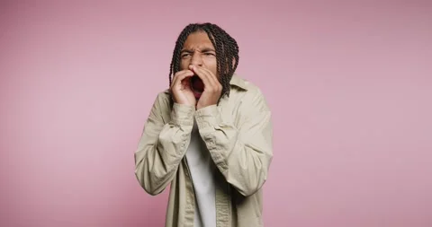 Man makes funny face while playing with mouth in studio with pink background 動画素材 326788308