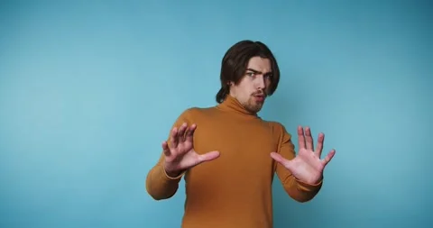 Man makes gestures in front of blue background while wearing a brown sweate.. Stockbeeldmateriaal 328249943