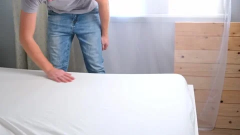 A man makes his cozy bed with fresh bright white bed linen. The day of the Stock Footage 222002908