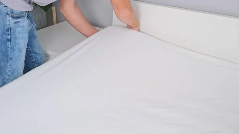 A man makes his cozy bed with fresh bright white bed linen. The day of the Stock Footage 229973068