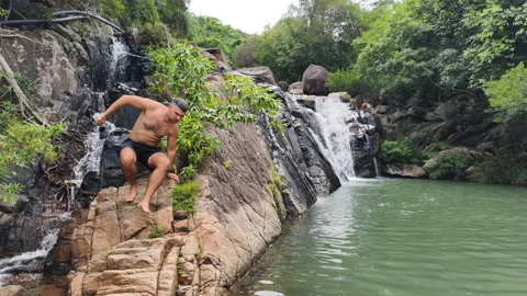 Man makes his way along rocks waterfall. Wilderness escape. Waterfall creates Stock Footage 322218104