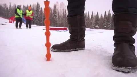 Man makes hole in snow with orange drill. People in uniform,trees in background. Stock Footage 157834876