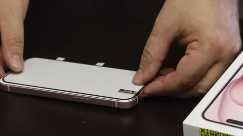 The man makes the installation of protective glass for iPhone 15. He fixes .. Stock Footage 277545959