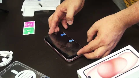 The man makes the installation of protective glass for iPhone 15. He fixes .. Stock Footage 277545962