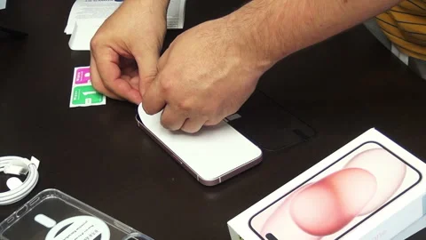 The man makes the installation of protective glass for iPhone 15. He fixes .. Stock Footage 277546023