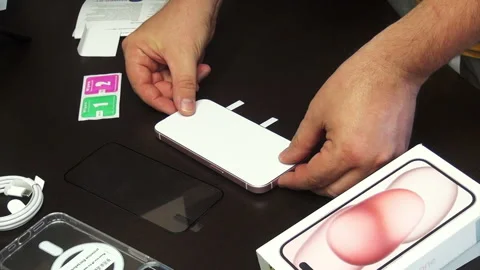 The man makes the installation of protective glass for iPhone 15. Fixes it .. Stock Footage 277546126