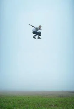 A man makes a massive jump in an empty field. he is flying in mid air! Stock Photos