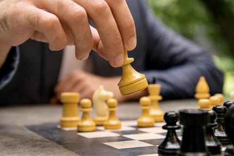 A man makes a move of a chess piece of a white queen on a board Stock Photos