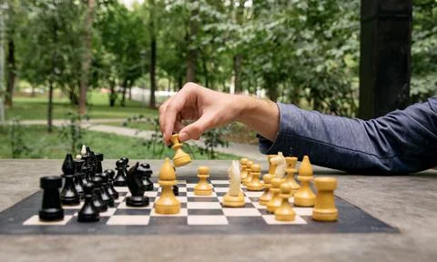 A man makes a move with a chess piece of a white queen, side view of the game Stock Photos