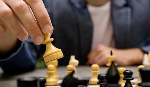 A man makes a move of a chess piece of a white queen on a board Stock Photos