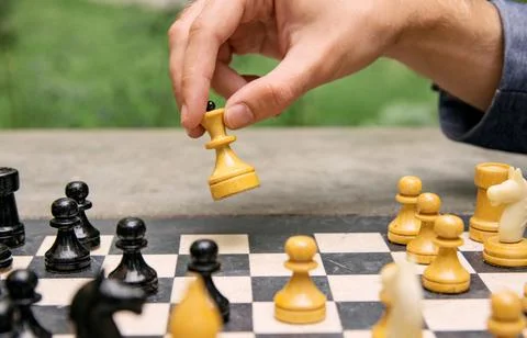 A man makes a move with a chess piece of a white queen, side view of the game Stock Photos