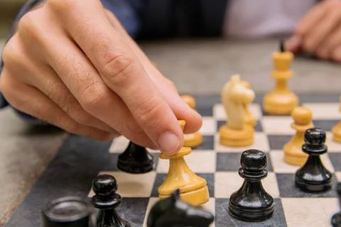 A man makes a move of a chess piece of a white queen on a board Stock Photos