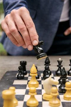 A man makes a move with a chess piece of a black knight on a board Stock Photos