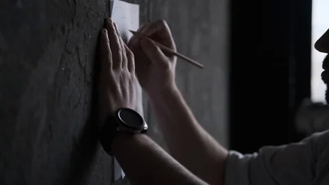 A man makes notes in a document by pressing a sheet of paper against a wall. Stock Footage 108616530