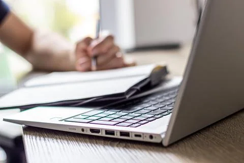A man makes notes in a notebook in front of laptop 스톡 사진