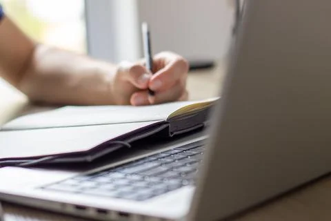 A man makes notes in a notebook ,typing in laptop ,at a table, image in light co Stock Photos