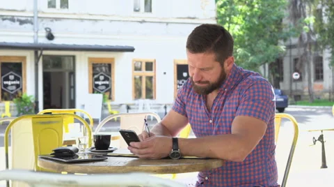Man makes notes from smartphone to notebook in cafe Vídeo Stock 67629190