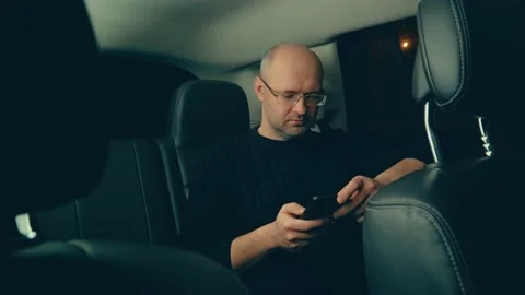 Man makes online purchases in app on mobile phone in back seat of SUV at night Stock Footage 172305571