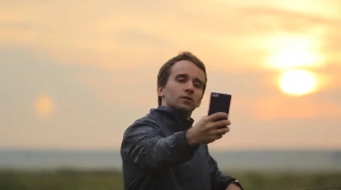 The man makes the photo on the smart phone. Beautiful sunset on the background Stock Footage 64600524