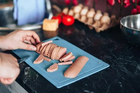Man makes pizza at home in the kitchen. Cuts the pizza sausage into strips Stock Photos