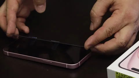 The man makes a protective glass installation for iPhone 15. He smoothes gl.. Stock Footage 277545877