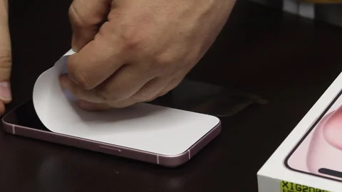 A man makes a protective glass installation for iPhone 15. Removes protecti.. Stock Footage 277545879