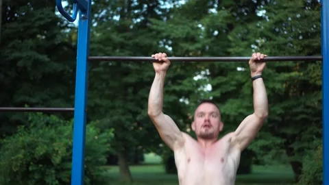 Man makes pull-ups on turnstile. Athletic guy pulls himself up on horizontal bar Stock Footage 164114074