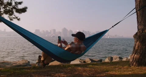 Man makes purchases on the Internet using a smartphone while lying in a hammock. Video stock 244399440