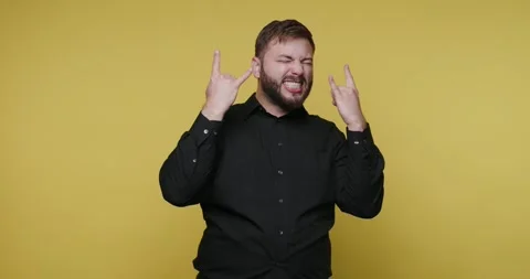 Man makes rock symbol with hands and sticks out tongue in front of yellow b.. Vídeos de archivo 326789891