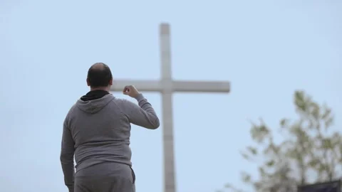 Man makes the sign of the cross in front of a large Christian cross, expressi Stock Footage 288412492
