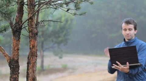 A man makes a video call on a laptop near a tree in the forest. Early morning Stock Footage 64594174