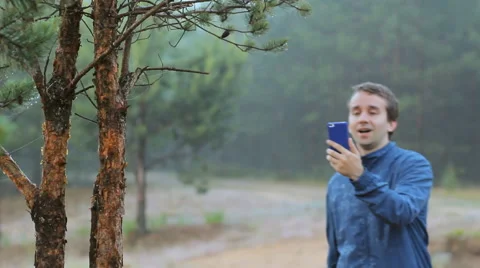 A man makes a video call by phone near a tree in the forest. Early morning Stock Footage 64597160