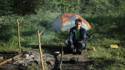 A man makes a video call on the tablet. Near the fire is burning and is tent  Stock Footage 64314318