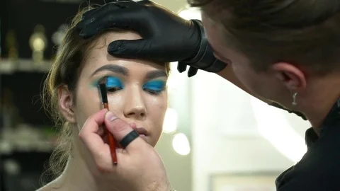 Man makeup artist making the face art with blue shadows in gloves Video stock 76570642