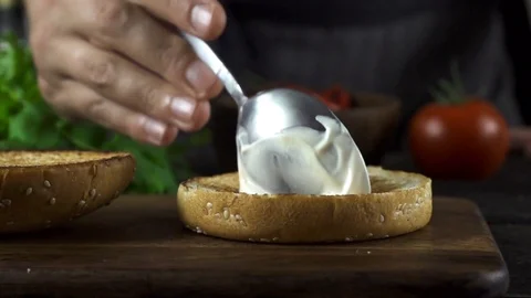 Man making burger in the kitchen and puts sauce with spoon 動画素材 104974584