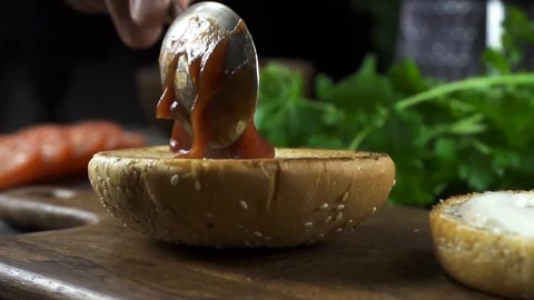 Man making burger in the kitchen and puts sauce with spoon Video stock 104974594
