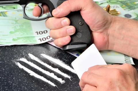 Man making cocaine lines using a white card and holding pistol gun in the other Stock Photos