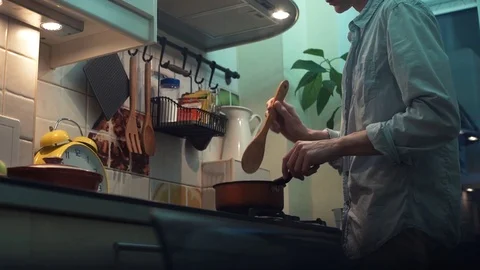 Man making dinner in pan on stove in kitchen. stirs wooden spoon Stock Footage 83088500