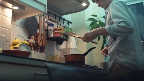 Man making dinner in pot on stove in kitchen. stirs wooden spoon Stock-Footage 83088243