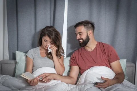 Man making fun laughing because his girlfriend crying while she reading a book Stock Photos