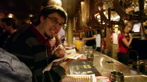 Man Making Funny Face While Looking at Menu at Beer Bar Counter Stock Footage 346638540