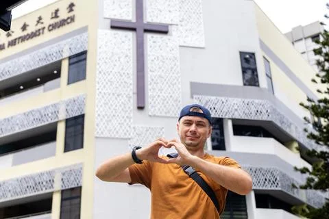 Man making heart gesture in front of modern church Stock Photos