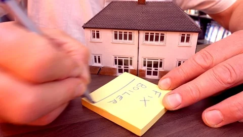 Man making a note to fix boiler, with a model house alongside. Stock Footage 93689295