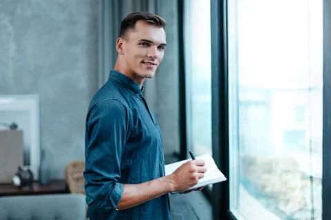 Man making notes in a notebook, standing near the window. Stock Photos