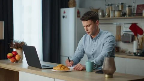 Man making notes working laptop in kitchen. Freelancer using wireless technology Stock Photos