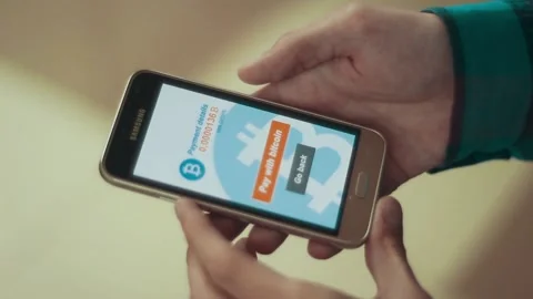 Man making a payment with bitcoins cryptocurrency using his smartphone Stock Footage 106670692